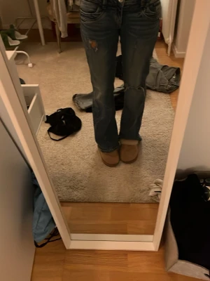 Blå bootcut jeans med slitningar - Säljer ett par blå jeans med bootcut passform och snygga slitningar på låret och knät. Jeansen har klassisk femficksdesign och låg midja. Materialet är robust denim som ger en cool och avslappnad vibe. Perfekta för dig som gillar en lite retro look. De är från Gina Tricot och jag har gjort hålen själv🩷de är i storlek 164 