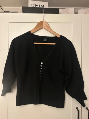 Svart kofta från Lindex med knappar - Svart kofta från Lindex i storlek S. Koftan har v-ringad hals och flera svarta knappar framtill. Materialet är stickat och modellen har lite loose passform med trekvartsärmar. 