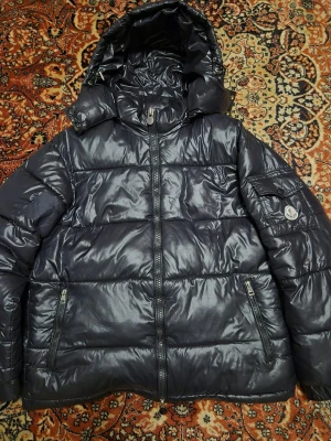 Svart pufferjacka från Moncler - NFC-taggen fungerar och skannar korrekt. Det finns en liten reva (visas på bilderna), men den påverkar inte slitage eller värme. Inga större fläckar eller skador utöver det. Levereras tvättad, ren och redo att användas 🧼✨ 📦 Skickas inom 24 timmar om möjligt 🚚⚡ Varm, glansig finish med den klassiska Moncler-logotypen på ärmen. Skicka ett meddelande för fler bilder eller information. #Moncler #MonclerJacket #MonclerPuffer #DesignerJacket #LuxuryStreetwear #WinterJacket #PufferJacket