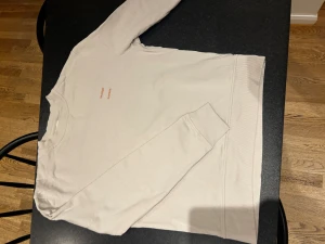 Beige sweatshirt från Samsoe Samsoe - Säljer en stilren beige sweatshirt från Samsoe Samsoe med diskret logga tryckt på bröstet. Tröjan har rund hals, långa ärmar och ribbade muddar vid ärmslut och nederkant. Perfekt för en chill och avslappnad look. Använd 1 gång 