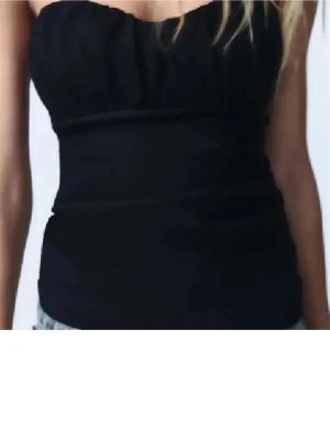 Svart bandeau tubtopp - Snygg svart bandeau tubtopp med lätt rynkad överdel och slät midja. Toppen är axelbandslös och har en stilren, enkel design som passar perfekt till jeans eller kjol. Materialet känns mjukt och följsamt mot huden.