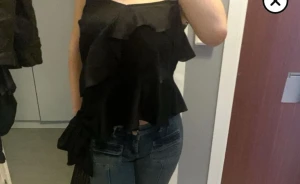 Svart volangig blus med smala axelband - Säljer en svart blus med smala axelband och flera lager volanger. Toppen har en luftig och flowy passform som ger en cool och trendig vibe. Perfekt att styla med jeans eller kjol för en snygg look. Materialet känns lätt och bekvämt mot huden. storlek M men har sytt banden så det passar mig som är xs