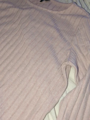 Ljusrosa ribbad tröja Vero Moda - Säljer en ljusrosa långärmad tröja från Vero Moda i storlek M. Tröjan har ett ribbat mönster och är tillverkad i mjukt material som känns skönt mot huden. Enkel rund halsringning och klassisk passform, perfekt för dig som gillar stilrena och softa plagg.