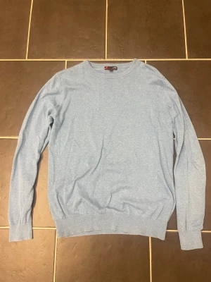 Ljusblå bomullströja från Dressmann - En stilren ljusblå tröja från Dressmann i mjuk pima bomull. Klassisk rund halsringning och ribbade muddar vid ärmslut och nederkant. Perfekt för dig som gillar enkel och clean stil.