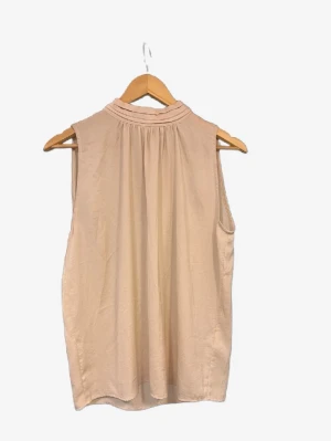 Beige blus från Saint Tropez - Säljer en stilren beige blus från Saint Tropez i storlek S. Blusen är ärmlös med hög krage och har ett mjukt, lätt material som ger ett snyggt fall. Perfekt att matcha med jeans eller kjol för en clean look.