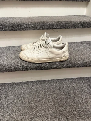 Valentino Garavani vita sneakers - Säljer ett par vita sneakers från Valentino Garavani med snygga silverfärgade nitar på hälen. Skorna har rund tå, snörning och är tillverkade i skinn. Klassisk och stilren design med diskret logga på plösen och mönstrade sömmar på ovansidan.