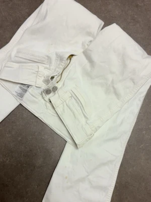 Vita bootcut jeans med knappar - Snygga vita jeans med bootcut.Tyvärr är det en fläck på dom som inte går bort!