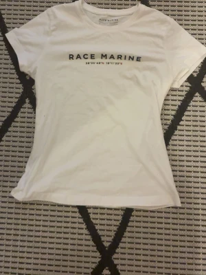 Vit t-shirt från Race Marine Xs - Vit t-shirt från Race Marine med tryck på bröstet och rund hals. Modellen är klassisk med korta ärmar och har en enkel, clean look. Materialet är mjuk bomull som känns skönt mot huden. Perfekt för dig som gillar sportig och stilren design. I storlek Xs