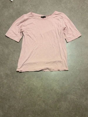 Ljusrosa t-shirt från Stockh lm - En enkel och mjuk ljusrosa t-shirt från Stockh lm i storlek S. T-shirten har rund hals och korta ärmar, tillverkad i bomull för en skön och avslappnad känsla. Perfekt att matcha med jeans eller shorts för en chill look.