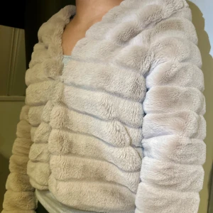 Beige pälsjacka med fluffig look - Supermjuk och fluffig beige pälsjacka med horisontella ränder. Jackan har långärmade ärmar och en croppad passform som ger en trendig vibe. Perfekt för dig som vill ha en cozy och snygg jacka med extra mycket fluff. 🤎🤎