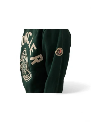 Grön sweatshirt från Moncler - Säljer en mörkgrön sweatshirt från Moncler med stort broderat logotyptryck på bröstet och ett klassiskt Moncler-märke på ärmen. Tröjan har långärmad design och är tillverkad i mjuk bomull för skön komfort. Perfekt för dig som gillar exklusiva streetwear-plagg.