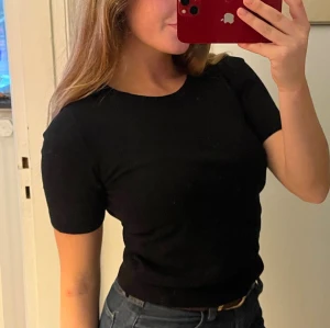 Svart tunt stickad topp med kort ärm - En stilren svart topp med rund hals och korta ärmar. Toppen är stickad och har en slim passform som sitter snyggt mot kroppen. Perfekt att matcha med jeans eller kjol för en enkel och clean look.