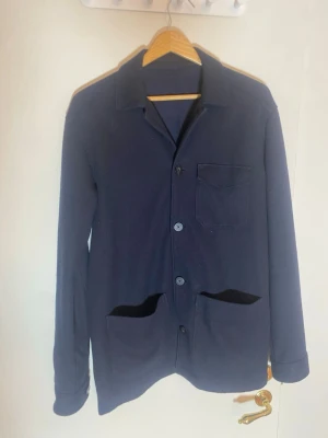 Mörkblå overshirt från Massimo Dutti - Snygg mörkblå overshirt från Massimo Dutti i ullblandat material. Jackan har klassisk krage, tre fickor framtill och knäppning med knappar. Perfekt att slänga över en hoodie eller t-shirt för en chill look.