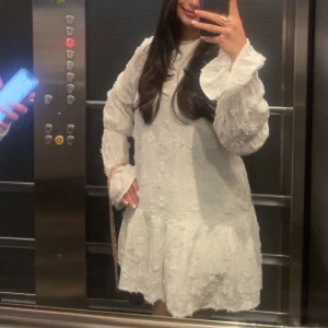 Vit blommig kortklänning med volang - Min fina studentklänning, den är vit å lagom kort med blommigt broderi över hela tyget. Klänningen har långa ärmar med volang vid ärmslut och en lätt rynkad kjol. Baksidan har en djupare urringning med knytband i nacken. Perfekt för dig som gillar romantisk och feminin stil. Har haft den på mig en gång och lyckats hålla den ren.