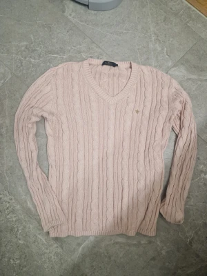 Ljusrosa stickad tröja Morris Lady - Snygg ljusrosa stickad tröja från Morris Lady i storlek M. Tröjan har ett klassiskt kabelstickat mönster, v-ringad hals och långärmade ärmar. Perfekt för dig som gillar preppy stil och mjuka material. Bleknat lite efter tvätt men knappt att den syns. Annars som ny.