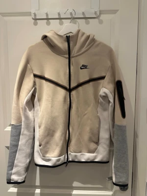 Beige Nike tech kofta - En beige Nike tech kofta i storlek xs. Koftan är väldigt skönt och sitter väldigt bra 