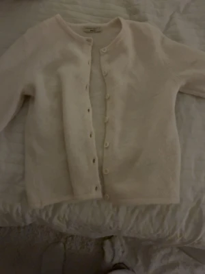 Beige stickad kofta från Gina Tricot - Mysig beige stickad kofta från Gina Tricot i storlek XS. Koftan har rund hals, långa ärmar och knäppning med vita knappar framtill. Perfekt att slänga på sig när det är lite kyligt ute. Stilren och enkel design som passar till allt.