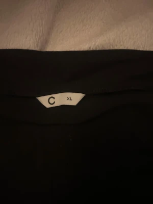 Svarta kostymbyxor från C i XL - Svarta yoga pants från C i storlek XL. Byxorna har en bred midja och rak passform, vilket ger en clean och stilren look. Materialet känns mjukt och har en lätt stretch, perfekt för dig som gillar att vara bekväm men ändå se snygg ut.