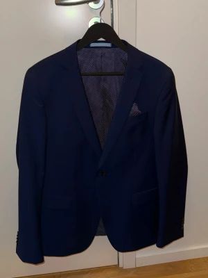 Marinblå kostym Sand Copenhagen strl 50 - Säljer en stilren marinblå kostym från Sand Copenhagen i storlek 50. Kostymen består av en kavaj med klassisk passform och matchande kostymbyxor. Materialet är 84% ull och 16% mohair, vilket ger en lyxig känsla och snygg struktur. Perfekt för dig som vill ha en elegant look. Endast använd 4-5 gånger. 