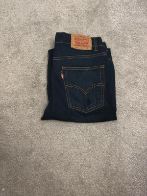 Levi's 517 mörkblå jeans - Säljer ett par Levi's 517 jeans i mörkblå tvätt med klassiska kontrastsömmar och fem fickor. Bootcut-modell med normal passform. Ikonisk läderpatch baktill och röd Levi's-tag på bakfickan. Perfekt för dig som gillar retrovibe och snygg siluett.