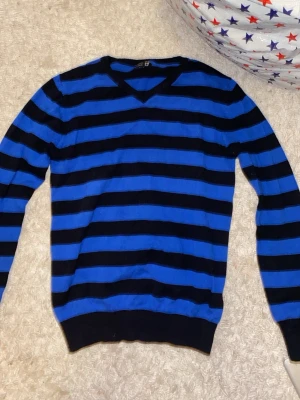 Blå och svart randig tröja BASIC U - Snygg långärmad tröja från BASIC U i storlek 158/164. Tröjan har ett randigt mönster i blått och svart, med v-ringad hals och ribbade muddar vid ärmslut och nederkant. Perfekt för dig som gillar stilrena och coola färgkombinationer.