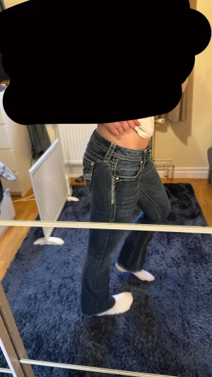 Mörkblå bootcut jeans från Rock Revival - Säljer ett par mörkblå jeans från Rock Revival med snygga kontrastsömmar och dekorativa fickor med broderi och knappar. Modellen har låg midja och bootcut-ben, vilket ger en riktigt schysst siluett. Klassiska jeansdetaljer och coola sömmar längs benen.     Kom privat för mer information🥰 säljer pga att de är förstora, och lite för korta i benen