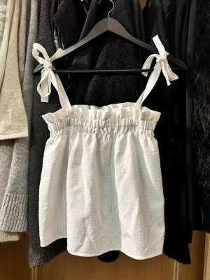 Topp med knytband - Så fin vit linnetopp med knytbara axelband och rynkad kant upptill. Perfekt till festtopp.