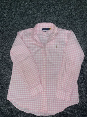 Rosa rutig skjorta från Polo Ralph Lauren - Säljer en klassisk rosa och vit rutig skjorta från Polo Ralph Lauren i bomull. Skjortan har lång ärm, button-down krage och broderad logga på bröstet. Perfekt för dig som vill ha en lite mer annorlunda färg på din Ralph lauren skjorta men ändå behålla stil och elegans, perfekt nu inför våren och sommaren. Storleken är M och skicket är riktigt bra. Priset går självklart att diskutera!. Tveka inte på att höra av dig vid minska lilla fundering så svarar jag så snabbt jag kan😄/Isak