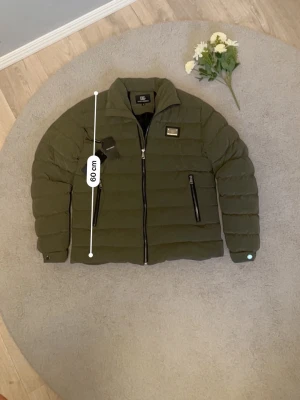 Olivgrön pufferjacka från Dolce & Gabbana - Säljer en stilren olivgrön Dolce & Gabbana jacka i storlek M. Jackan är perfekt till vintern då den är varm, bekväm och samtidigt snygg att bära till både vardag och mer uppklädda outfits. Den är i mycket fint skick och sparsamt använd. Längden är cirka 60 cm. Jag är aktiv på Plick och fraktar samma dag vid snabb affär. Hör gärna av dig om du har frågor eller vill ha fler bilder✅📦🚚😊
