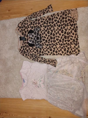 Leopardmönstrad långärmad klänning - Säljer en beige långärmad klänning med svart leopardmönster och en stor rosett framtill. Klänningen har rund hals och är i mjukt material, perfekt för dig som gillar djurmönster och vill sticka ut.