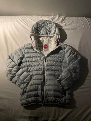 Colmar jacka  - Säljer en ljusgrå pufferjacka från Colmar med huva och dragkedja. Jackan har quiltad design, två fickor med dragkedja och klassisk Colmar-logga på ärmen. Perfekt för kyliga dagar.