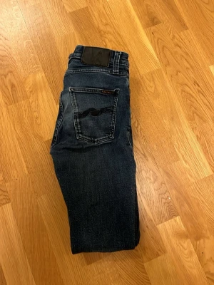 Nudie jeans pipe led  - Säljer ett par mörkblå  jeans från Nudie Jeans i modellen pipe led den har en klassisk broderad bakficka och svarta detaljer vid linningen. Jeansen har en smal passform och är tillverkade i slitstarkt denimtyg med snygga tvättade effekter. Perfekt för dig som gillar en tajt look. W30 L34