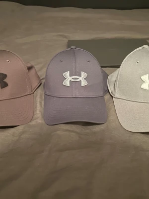 Grå dunväst från Under Armour - Snygg grå dunväst från Under Armour med klassisk logga framtill. Västen har en stilren design med rundad hals och raka linjer. Materialet är mjukt och lätt, perfekt för lager-på-lager. Passar dig som gillar sportig och clean stil.