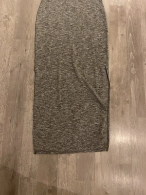 Grå långkjol från Gina Tricot - Säljer en gråmelerad långkjol från Gina Tricot i storlek M. Kjolen har en rak och tight passform med bred resår i midjan för extra komfort. Materialet är en mix av polyester, viskos och elastan som gör den mjuk och stretchig. Perfekt för dig som gillar enkel och stilren look.