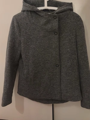 Grå kappa från ONLY - Säljer en grå kappa från ONLY i storlek S. Jackan har huva, knappar framtill. Den är används fåtal gånger men ser ut o vara i nytt skick 