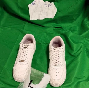 Nike Air Force 1 vita sneakers - Säljer ett par klassiska Nike Air Force 1 sneakers i helvitt skinn med perforerad tå och rund sula. Skorna har snörning och lågt skaft, med den ikoniska swoosh-loggan på sidan. Perfekt för dig som gillar stilrena och tidlösa sneakers.