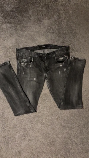 Replay jeans  - Säljer ett par svarta Replay jeans med slim, lite rak beroende på stl, och slitna detaljer på framsidan. Jeansen har klassisk femficksdesign, stretchigt material och snygga sömmar på bakfickorna. Perfekta för dig som gillar en smal siluett och streetstil.