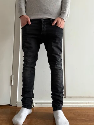 Svarta slim fit jeans från Jack & Jones - Säljer ett par svarta skinny jeans från Jack & Jones Jeans Intelligence. Jeansen har en tight passform, klassisk femficksdesign och är tillverkade i stretchig bomullsmix för extra komfort. Snyggt tvättade detaljer och normal midja.W29 L30