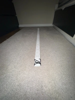 Vitt bälte med monogrammönster & silver spänne - Vit bälte med ikoniskt monogrammönster och svart metallspänne. Stilren och lätt att matcha till både vardag och fest. Snygg detalj som lyfter vilken outfit som helst.