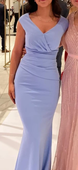 Festklänning/balklänning - Supersnygg ljusblå långklänning från Goddiva med v-ringning och omlott-detalj upptill som för midjan att se smal ut. Klänningen är ärmlös och har en figurnära passform som framhäver siluetten. Perfekt för bal, fest eller bröllop! Materialet är mjukt och stretchigt polyester.