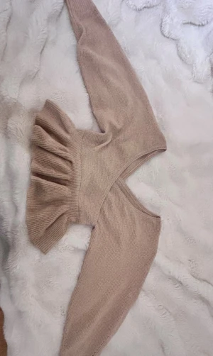 Beige stickad omlottopp från ASOS - Säljer en beige stickad omlottopp från ASOS DESIGN med volangdetalj nedtill. Toppen har långärmade ärmar och v-ringad hals. Materialet är mjukt och ribbat, perfekt för att ge en chill och snygg vibe till din outfit.