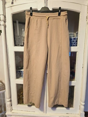 Beige mjukisbyxor från Flattop M - Säljer ett par beige mjukisbyxor från Flattop i storlek M. Byxorna har en avslappnad passform med snörning i midjan och praktiska sidofickor. Materialet är mjukt och skönt, perfekt för chill dagar. Snyggt gulvitt snöre i midjan för extra detalj. Petit modell