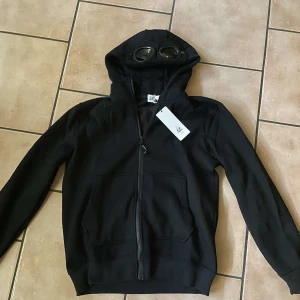 Svart hoodie från C.P. Company - Säljer nu min C.P. Company hoodie då den inte passar. Det är en väldigt skön hoodie med fint material. Finns qr kod som du kan se på bild 3. Tagsen sitter inte kvar tyvärr.