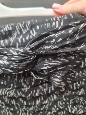 Svart och vit mönstrad kortkjol - Säljer en svart och vit kortkjol med coolt abstrakt mönster. Kjolen har snygga rynkade detaljer och en dragkedja bak. Materialet känns lätt och skönt, perfekt för dig som gillar att sticka ut med din stil.