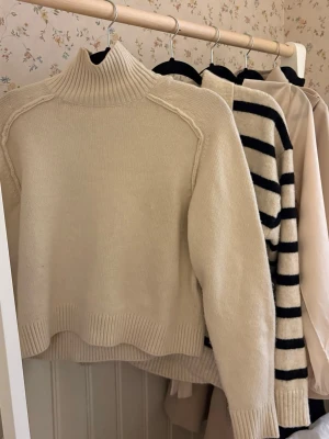 Beige stickad polotröja - Säljer en beige stickad polotröja med hög krage från H&M . Tröjan är lite åt det kortare hållet, slutar ungefär vid mitten av rumpan. Perfekt för kyliga dagar!