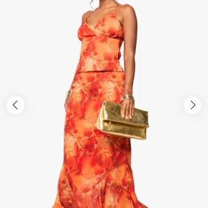 Orange och röd blommig sett med korsett topp och maxikjol. - Snygg sett i orange och röda toner med blommigt mönster. Klänningen har smala axelband, v-ringad urringning och figurnära passform upptill. Köpt för 450kr på rea. Kjolen är i storlek 36 och toppen i storlek 38. Aldrig använt prislapp finns kvar. Pris kan diskuteras!