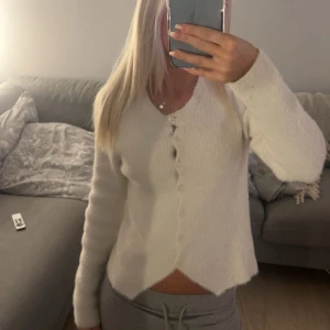 Vit fluffig kofta från Stradivarius - Supermjuk och fluffig vit kofta från Stradivarius med rund halsringning och pärlemorknappar. Koftan har lång ärm och är stickad i ett lurvigt material som känns extra mysigt. Perfekt att slänga på sig när det är kyligt ute.