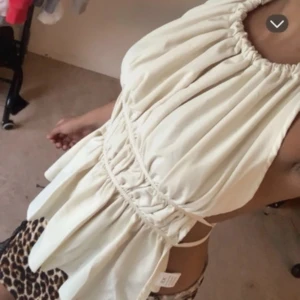 Beige omlott linnetopp med snörning - Säljer en beige omlott linnetopp med snygga snörningsdetaljer i midjan och öppen rygg. Toppen har en luftig och flowy passform, är ärmlös och knyts i nacken och ryggen. Perfekt för varma dagar och ger en trendig look.