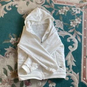 Stilren och fett skön vit cardigan - Säljer en stilren vit cardigan med dragkedja och huva. Jackan har långa ärmar och ribbade muddar vid ärmslut och nederkant. Perfekt för en avslappnad look. Skriv ifall du har frågor eller för mer bilder!🙌🏻