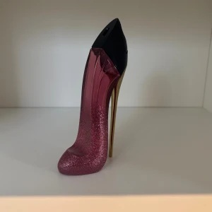 Carolina Herrera - Snygg parfymflaska i form av en rosa glittrig högklackad sko med gulddetaljer. Perfekt för dig som vill ha en unik och trendig accessoar på sminkbordet. Flaskan har Carolina Herreras logga på toppen. FLASKAN ÄR TOM SÄLJER BARA FLASKAN INGET INNEHÅLL!